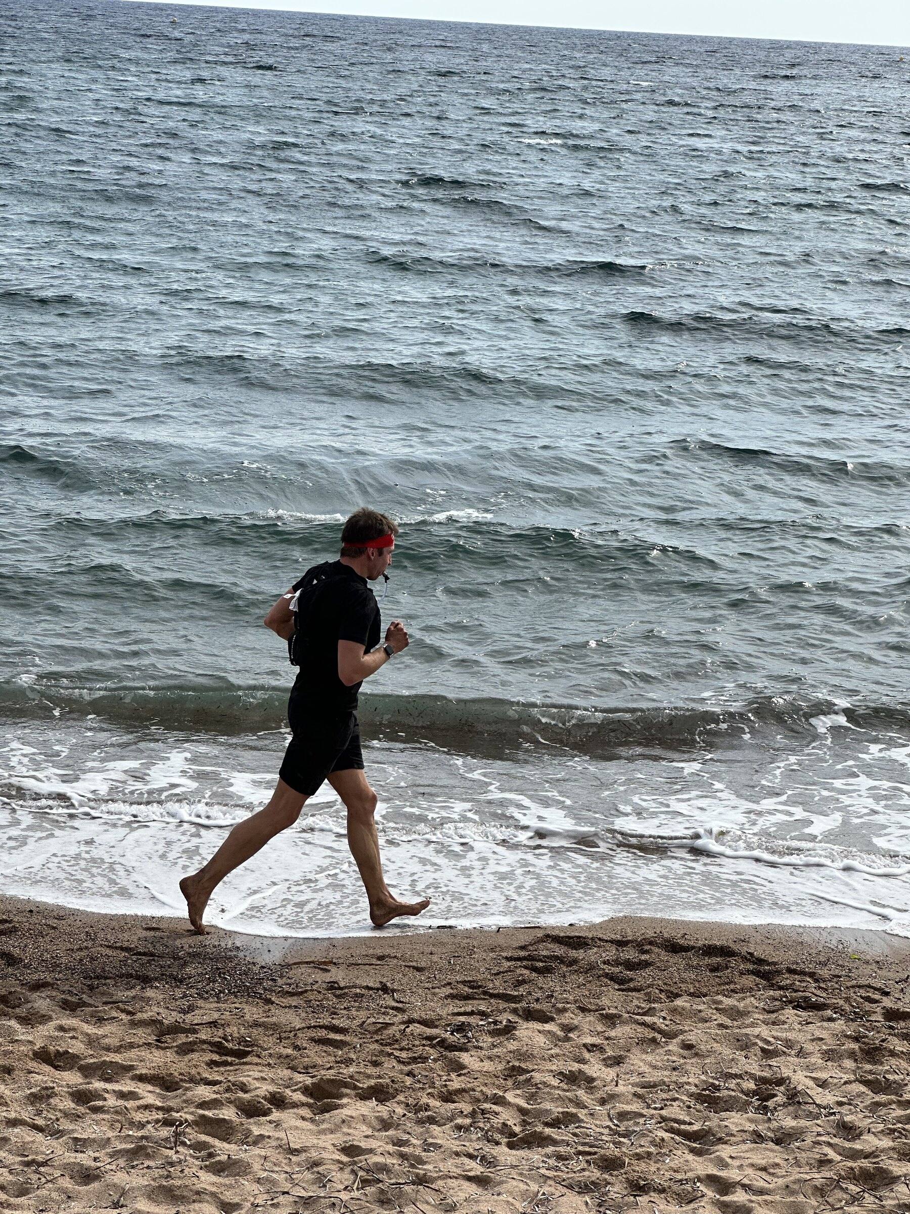 Antoine court pieds nus sur le sable au bord de la Méditerranée, en tee-shirt et short noirs